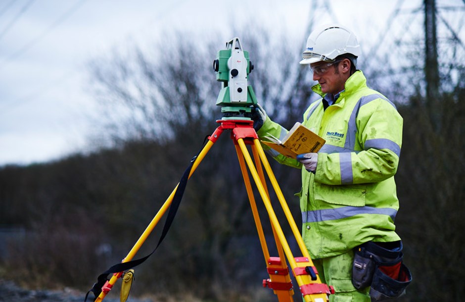 A construction worker in a hard hat and hi-vis working with a piece of surveying equipment