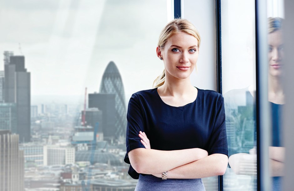 Professional female standing in front of glass window with London skyline behind