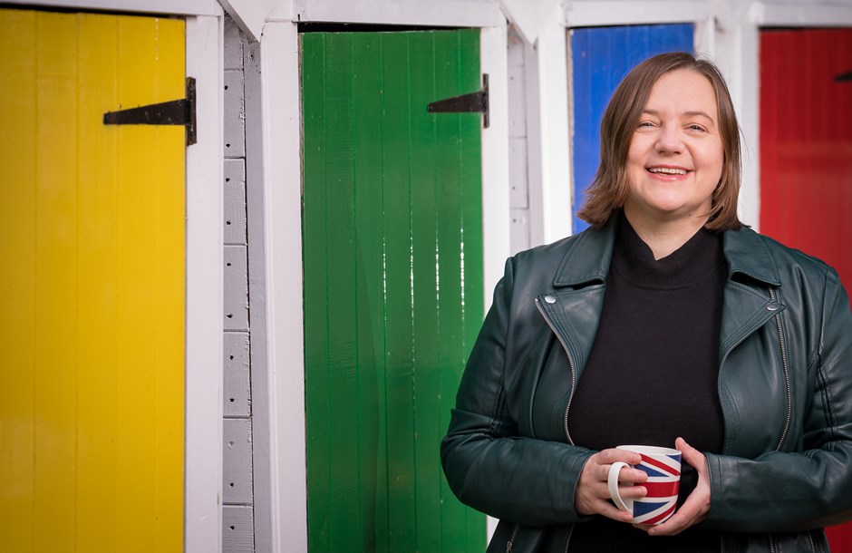 Paula McMahon of Sir Robert McAlpine standing in front of a colourful set of doors, holding a mug 